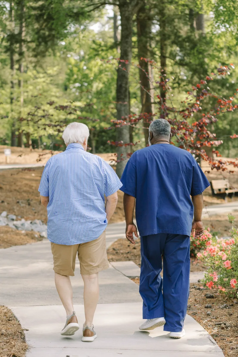 DayBreak caregiver walking with an older adult through a familiar outdoor setting