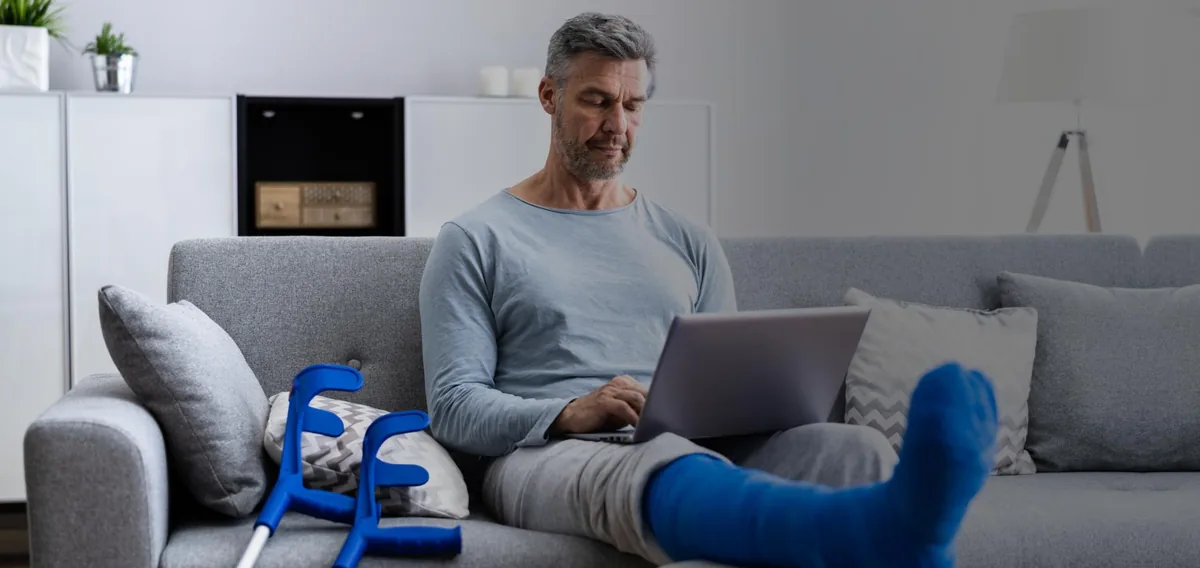 Adult recovering at home after surgery with a leg cast and crutches nearby